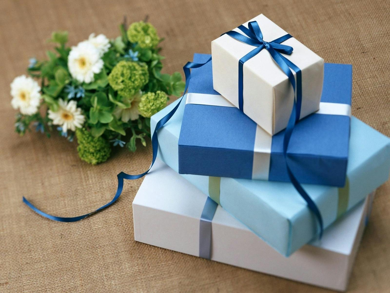 Three beautifully wrapped gift boxes with blue ribbons arranged beside a floral bouquet.